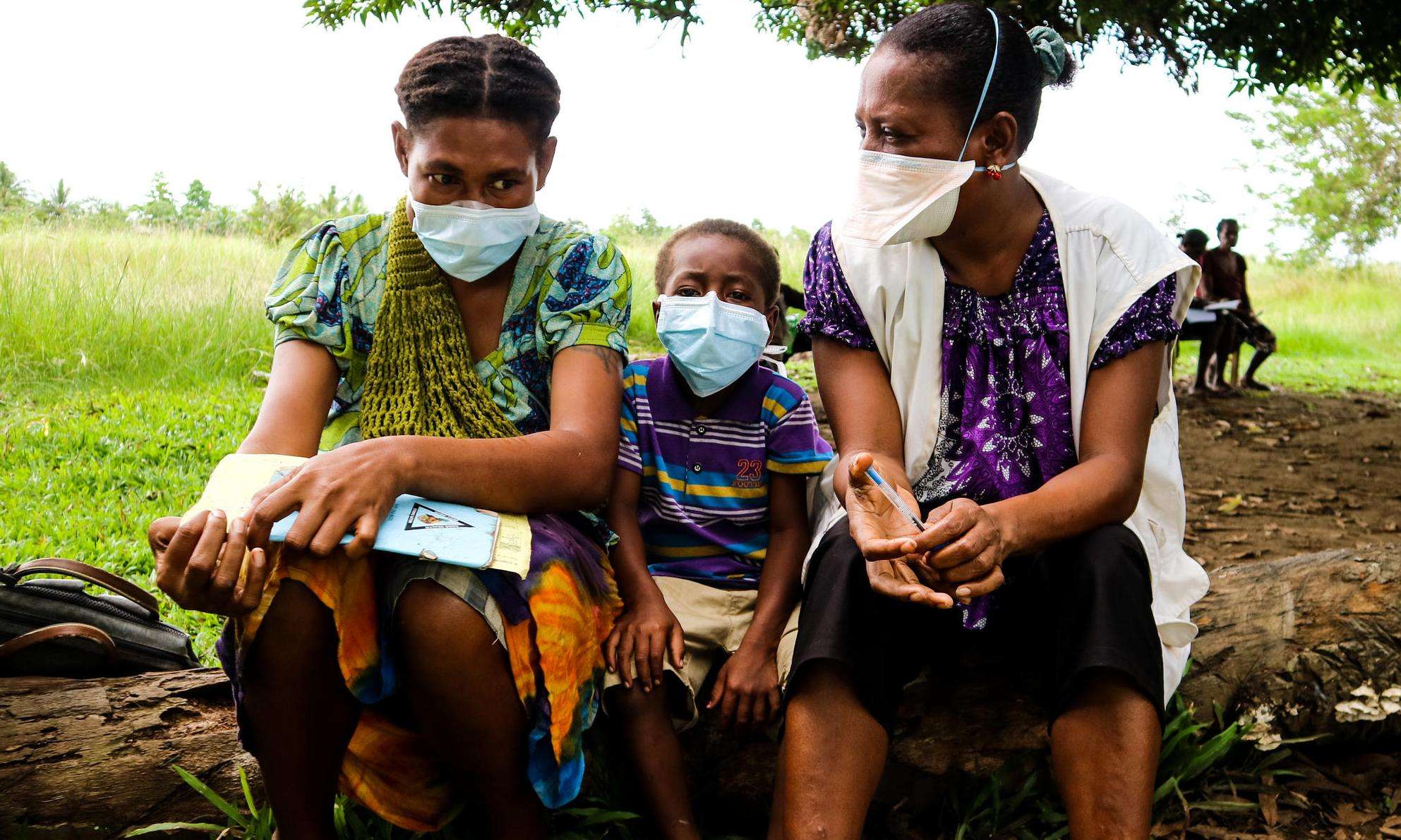 A child sits between two people in surgical masks after completing TB treatment from MSF in Papua New Guinea.