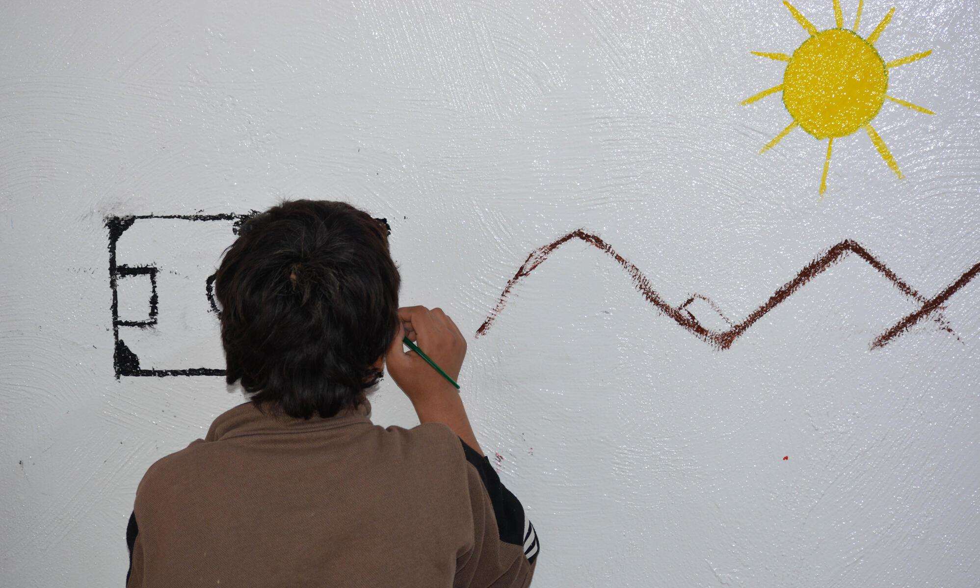 A child draws a sun and mountains on the wall during an art therapy session in Al-Hol camp, northeast Syria.