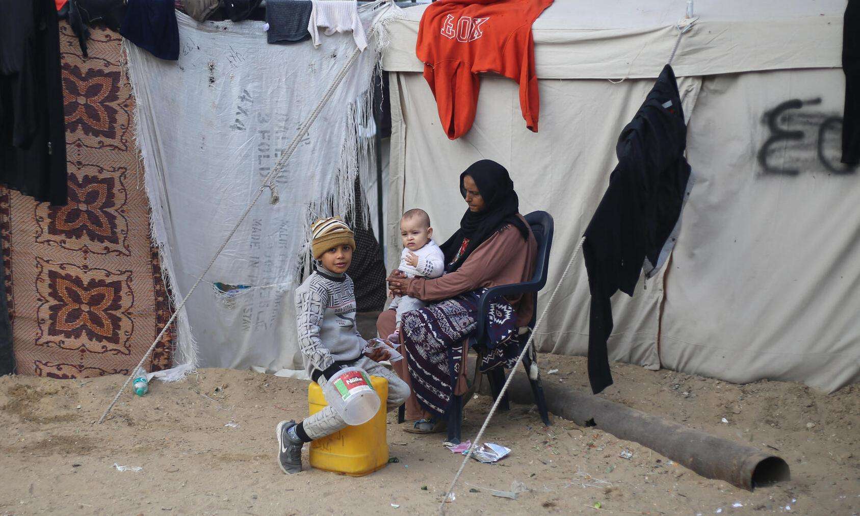 A displaced Palestinian woman with her children outside a makeshift tent in Gaza.