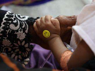 A child's hand with smiley face sticker holding an adult's hand with embroidered sleeve in Yemen
