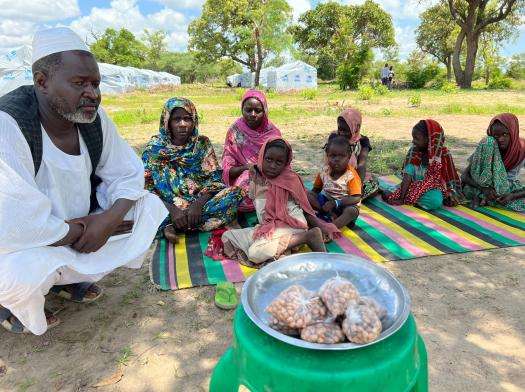 Sudanese man with family sitting on ground outside refugee camp in Central African Republic
