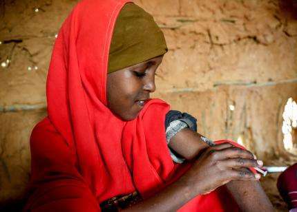 A young girl in a red headscarf injects insulin in Kenya.
