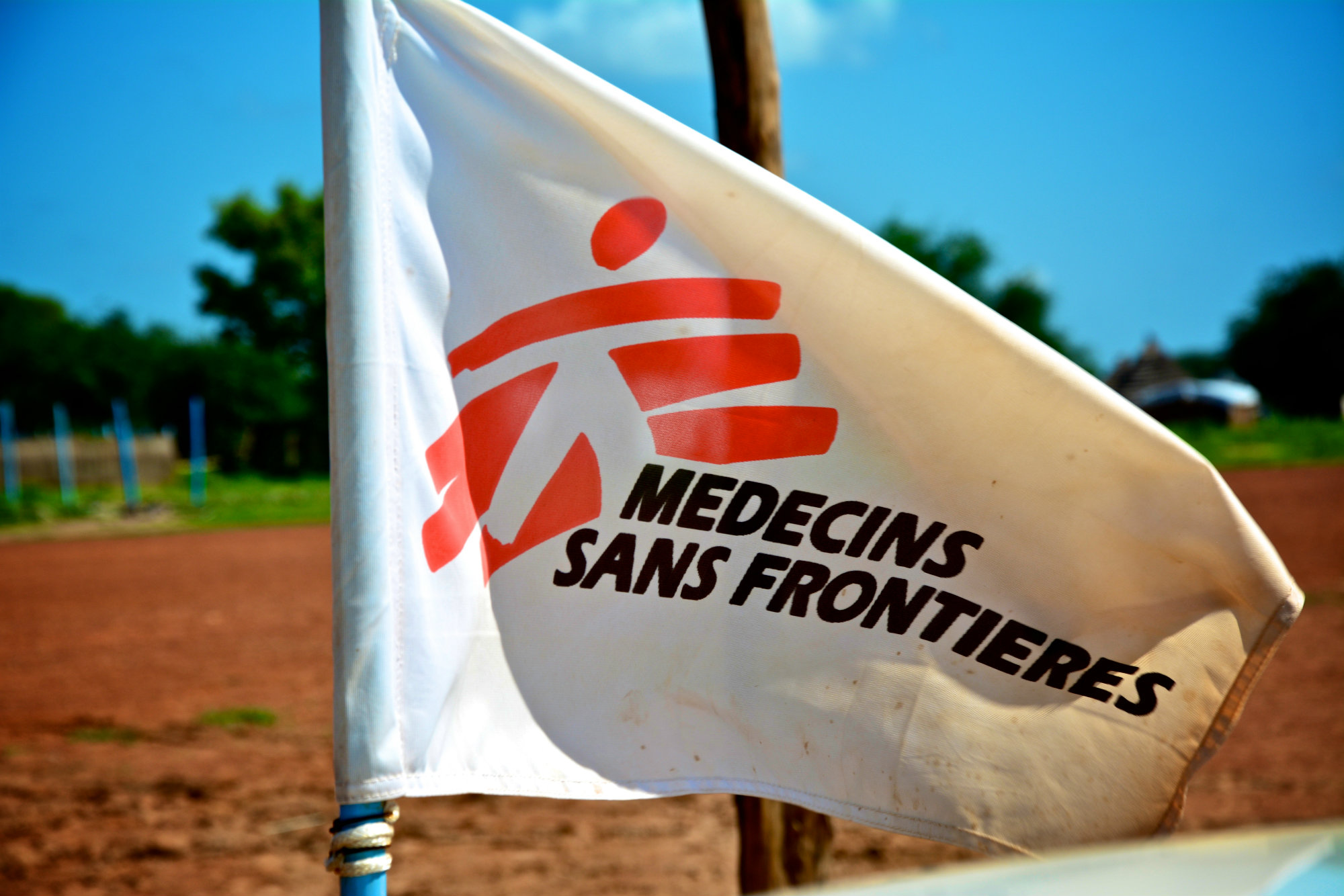 White flag with red logo of Doctors Without Borders/Médecins Sans Frontières (MSF) against sunny blue sky