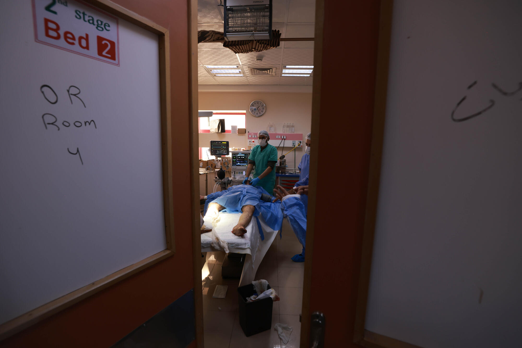 Open door to an operating room at Al Aqsa Hospital in Gaza, as doctors perform surgery on a patient.