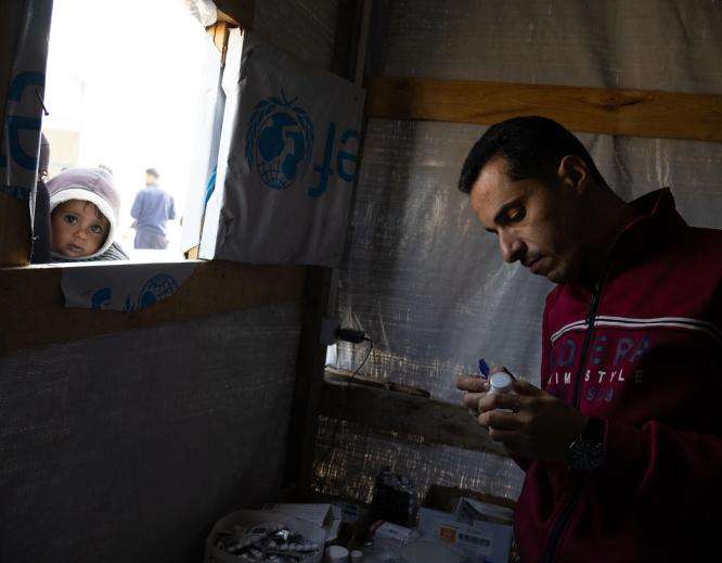 A man looks at notes as a child looks through the window of a clinic in Gaza.