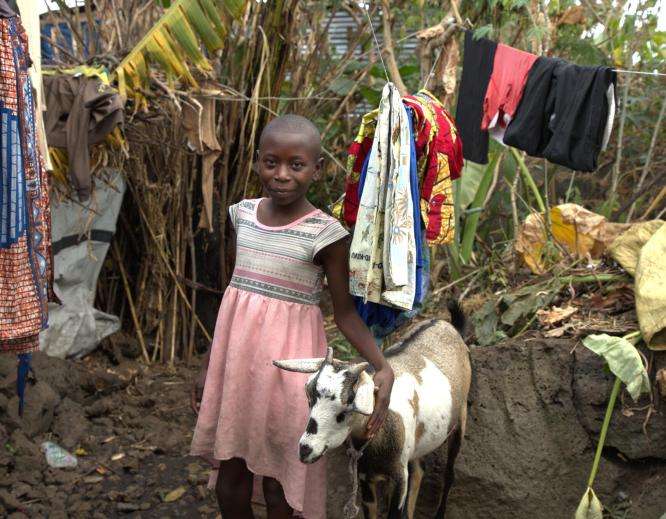 A girl stands next to a goat and smiles at the camera in DR Congo. 