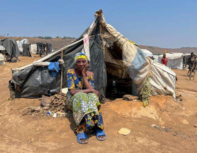 A woman sitting in front of a tent looks at camera in Burundi. 