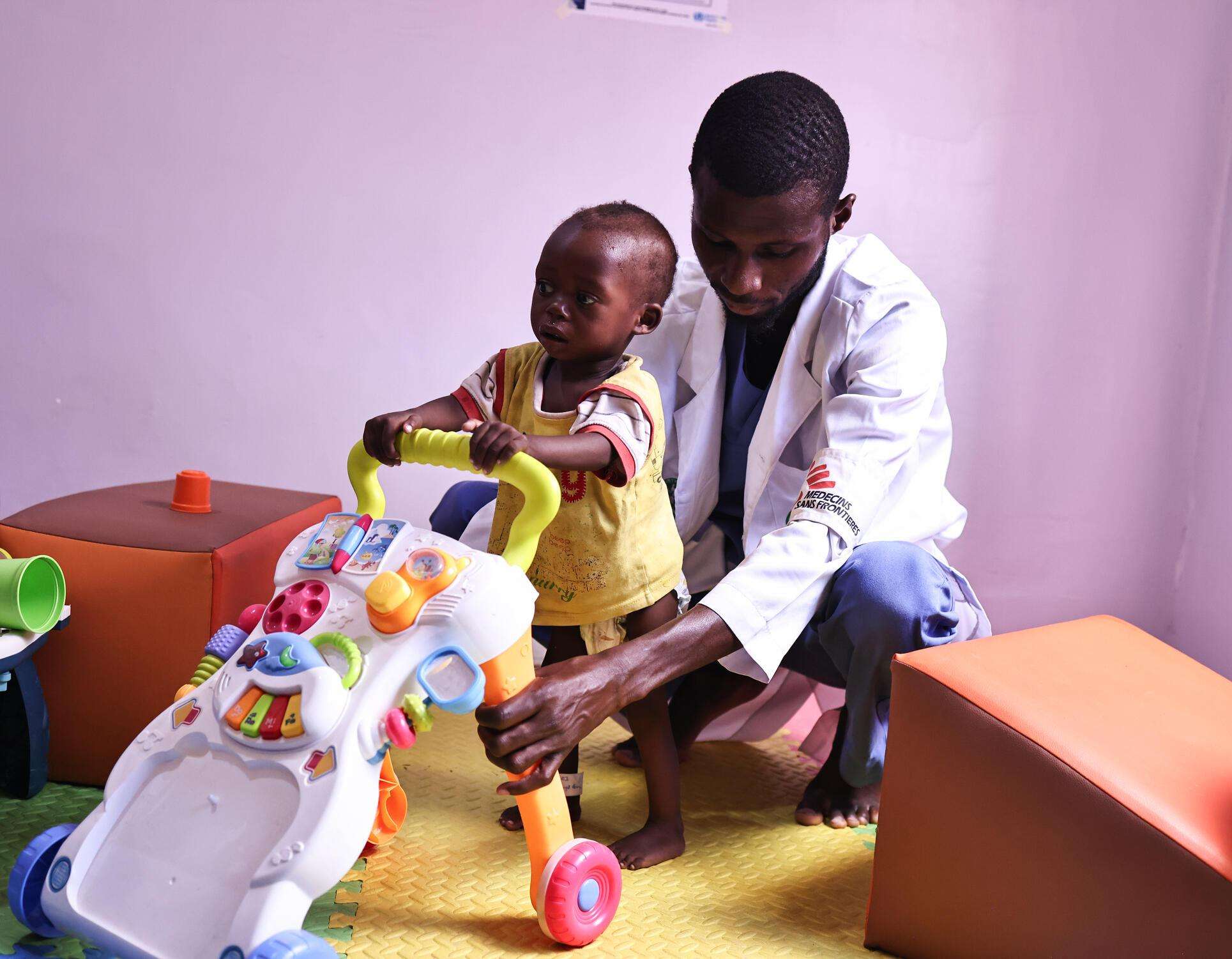 MSF physiotherapist Mubarak guides Usman, a 13-month-old child, walk with the aid of a plastic push-toy during a group session with tje caregivers of children suffering from malnutrition in Kano state, Nigeria