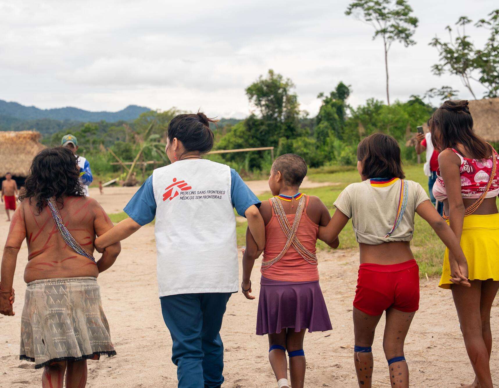An MSF worker links arms with Yanomami community members in Brazil. 