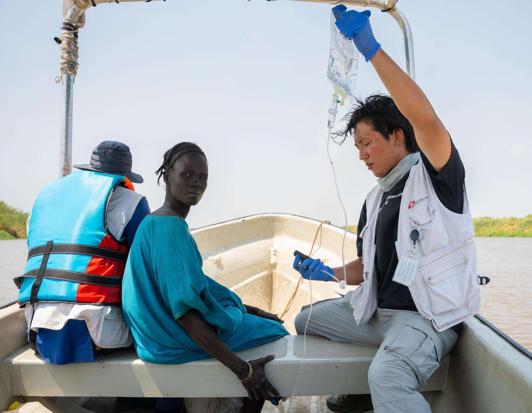 MSF staff member Joon Hyun holds an IV drip for a patient as she is transported to Chuil primary health care center from a mobile clinic in Yakuach.