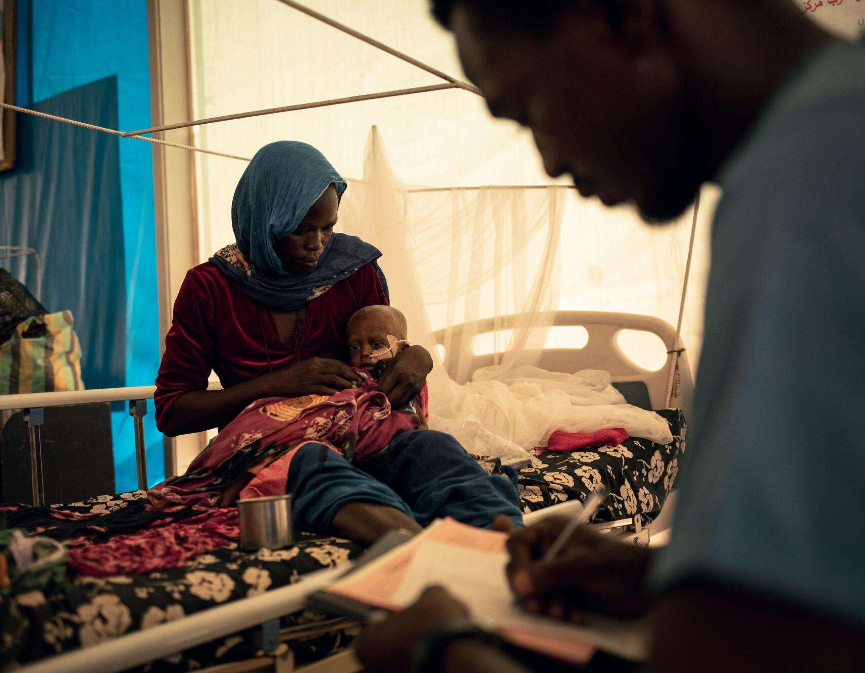 A woman holds her infant son on her lap in a hospital bed in Chad. 