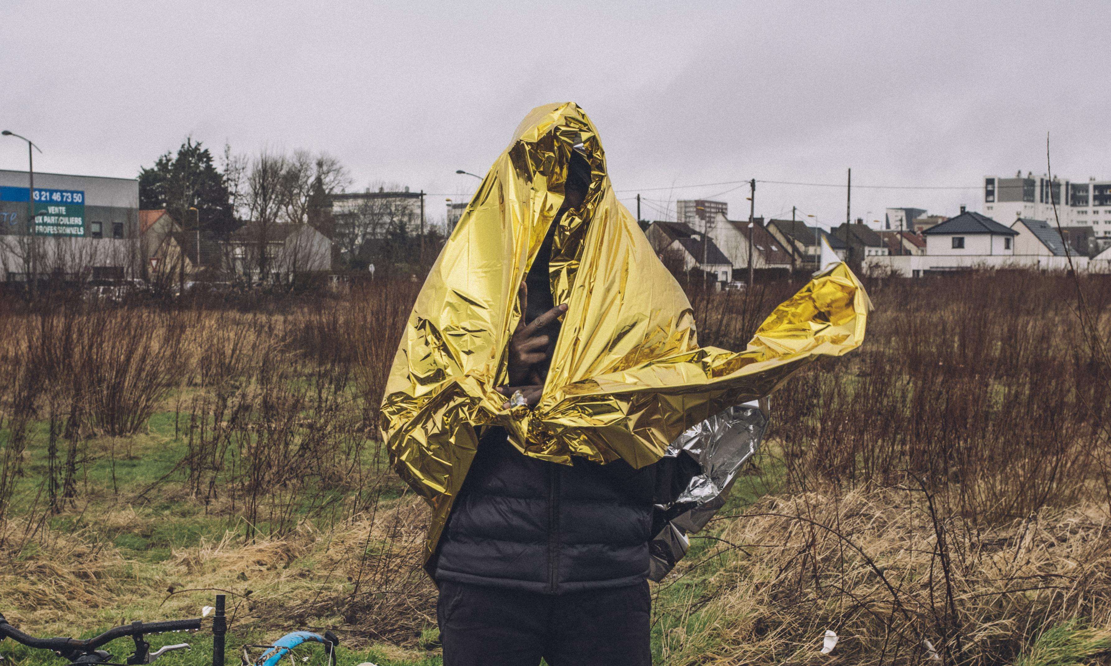 A young migrant covers himself with a survival blanket on a rainy day in Calais.