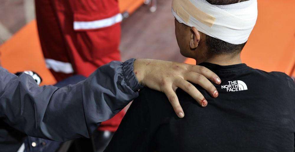 A man puts his hand on his injured friend's shoulder in support.