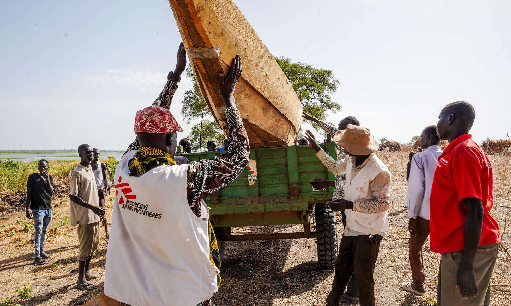 People wearing white vests with MSF logo remove canoe from tractor in Dentiuk, South Sudan