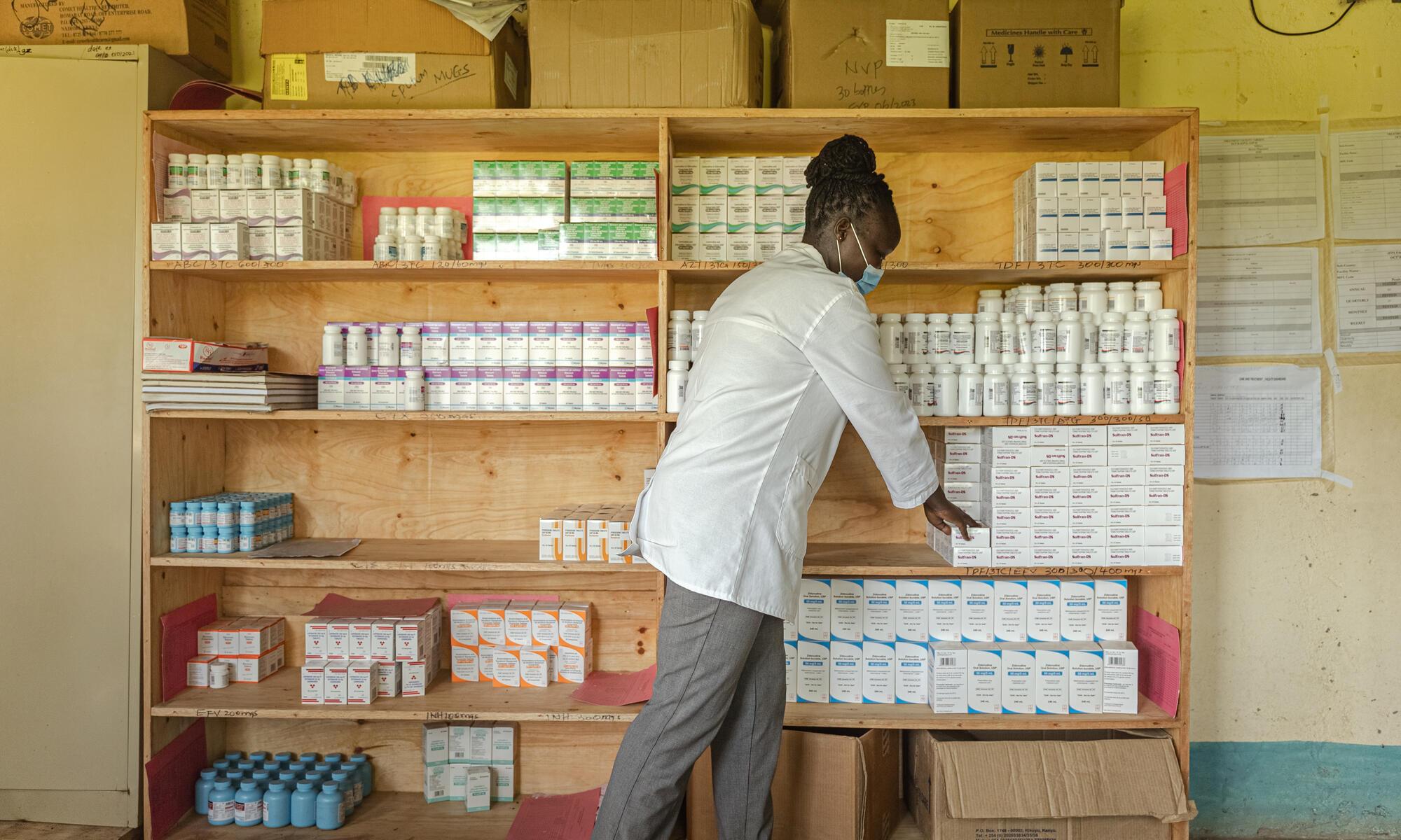 An MSF clinician in white coat picking ARVs out of boxes for a patient.