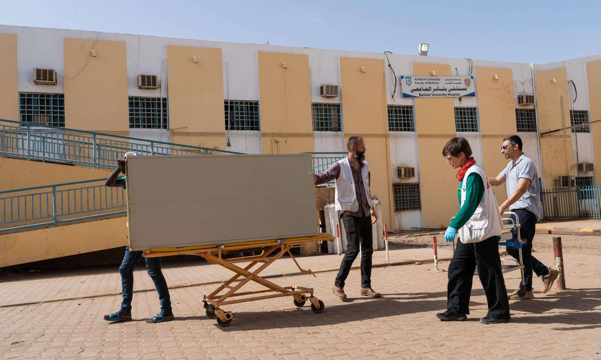 A group of MSF staff push a large object on wheels in front of a yellow building in Khartoum, Sudan.