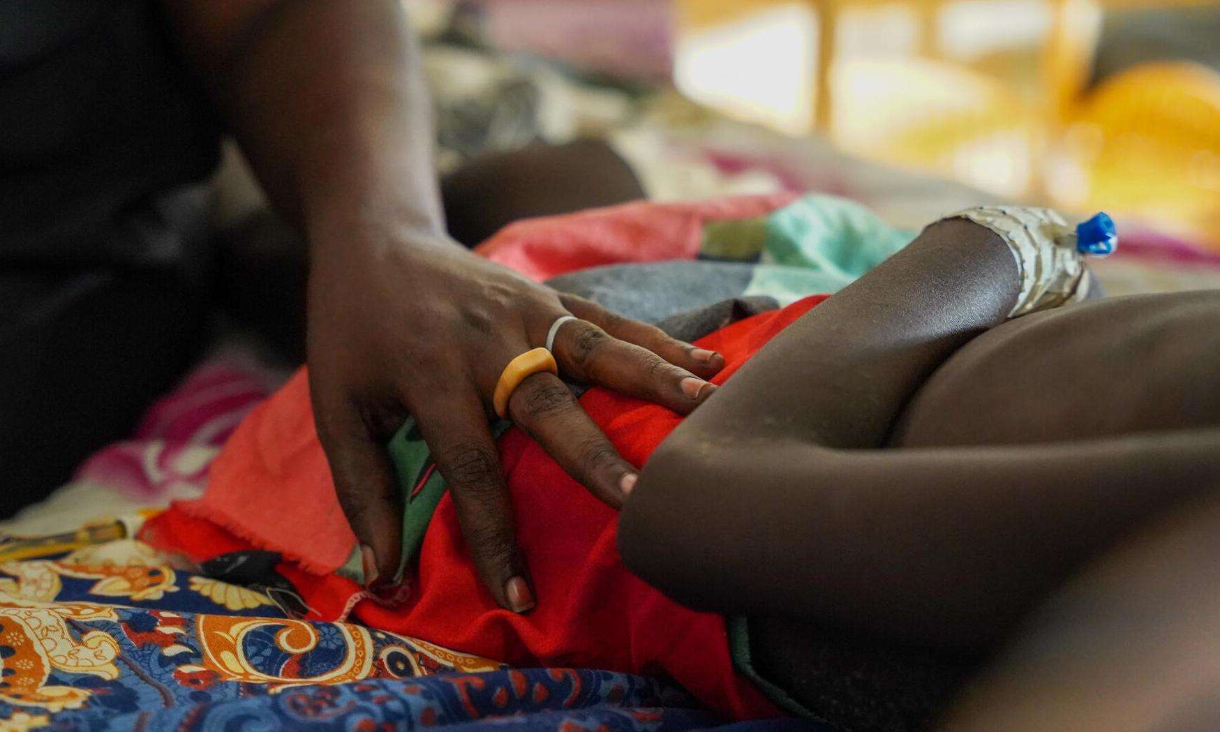 A woman lays her hand on a child lying in a pediatric ward with measles at MSF's facility in Bentiu camp, South Sudan.