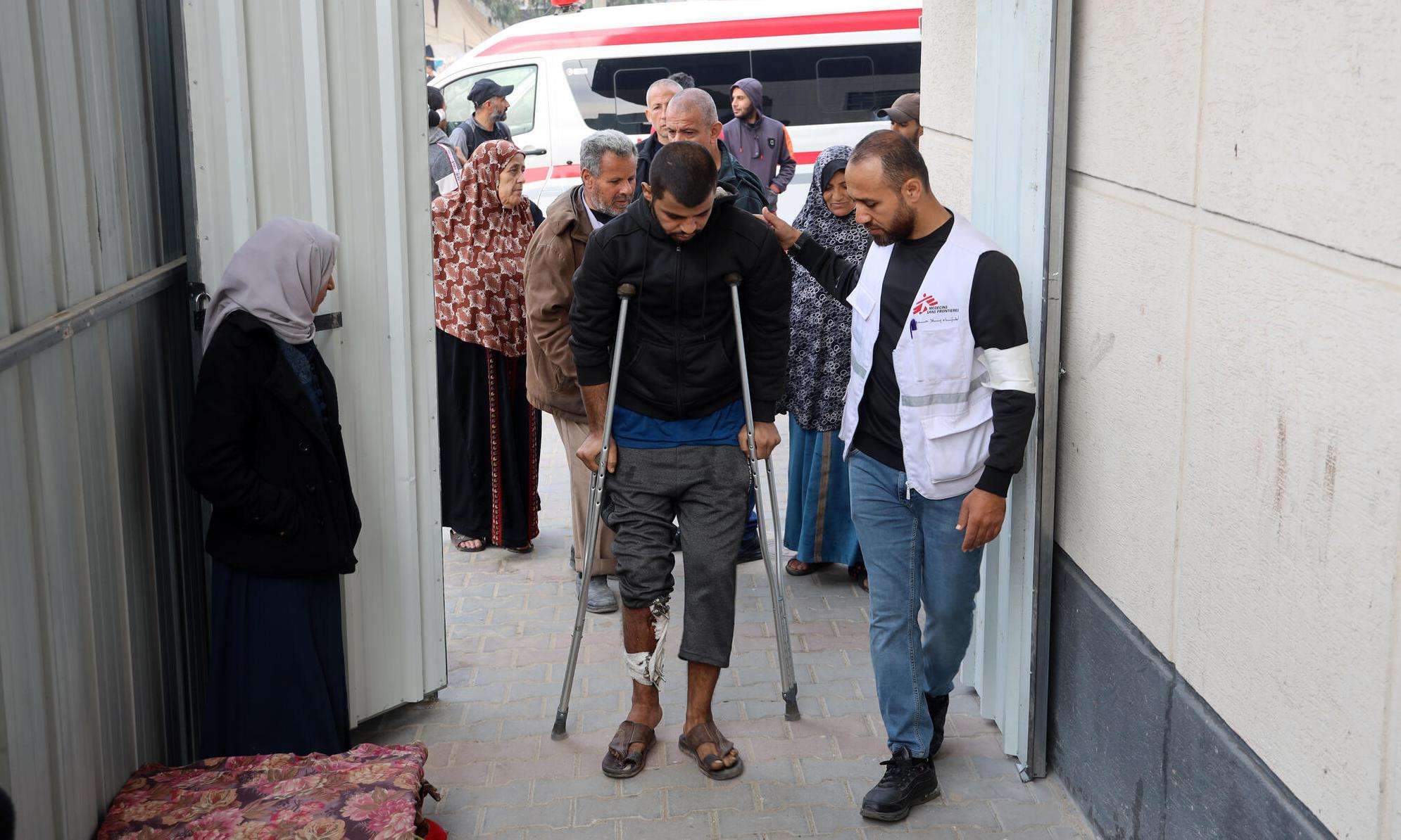 An MSF staff member helps an injured man on crutches at Rafah Indonesian Hospital in southern Gaza.