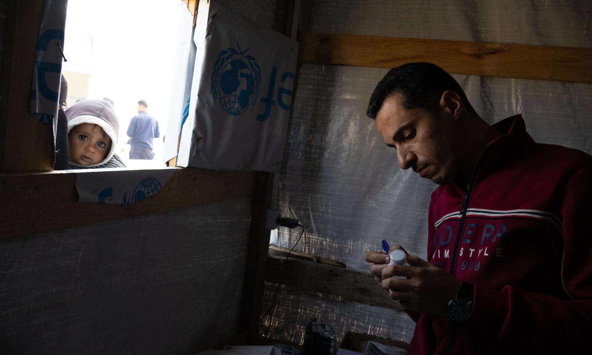 A man looks at notes as a child looks through the window of a clinic in Gaza.