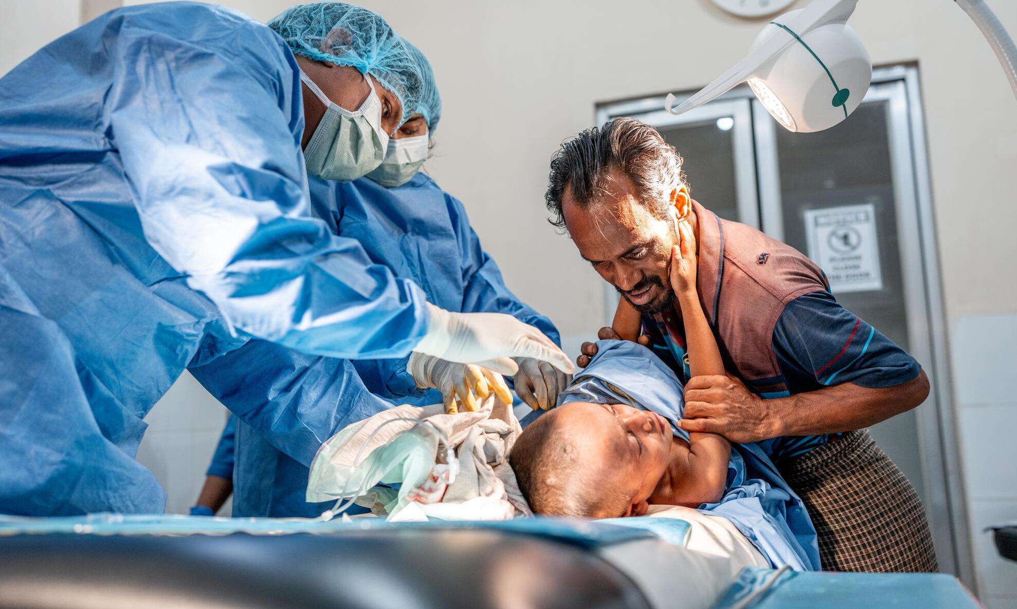 Anis Mohammad tries to comfort his 4-year-old son, Shofi, as he receives treatment for multiple abscesses in the emergency room at MSF's Kutupalong Hospital. 