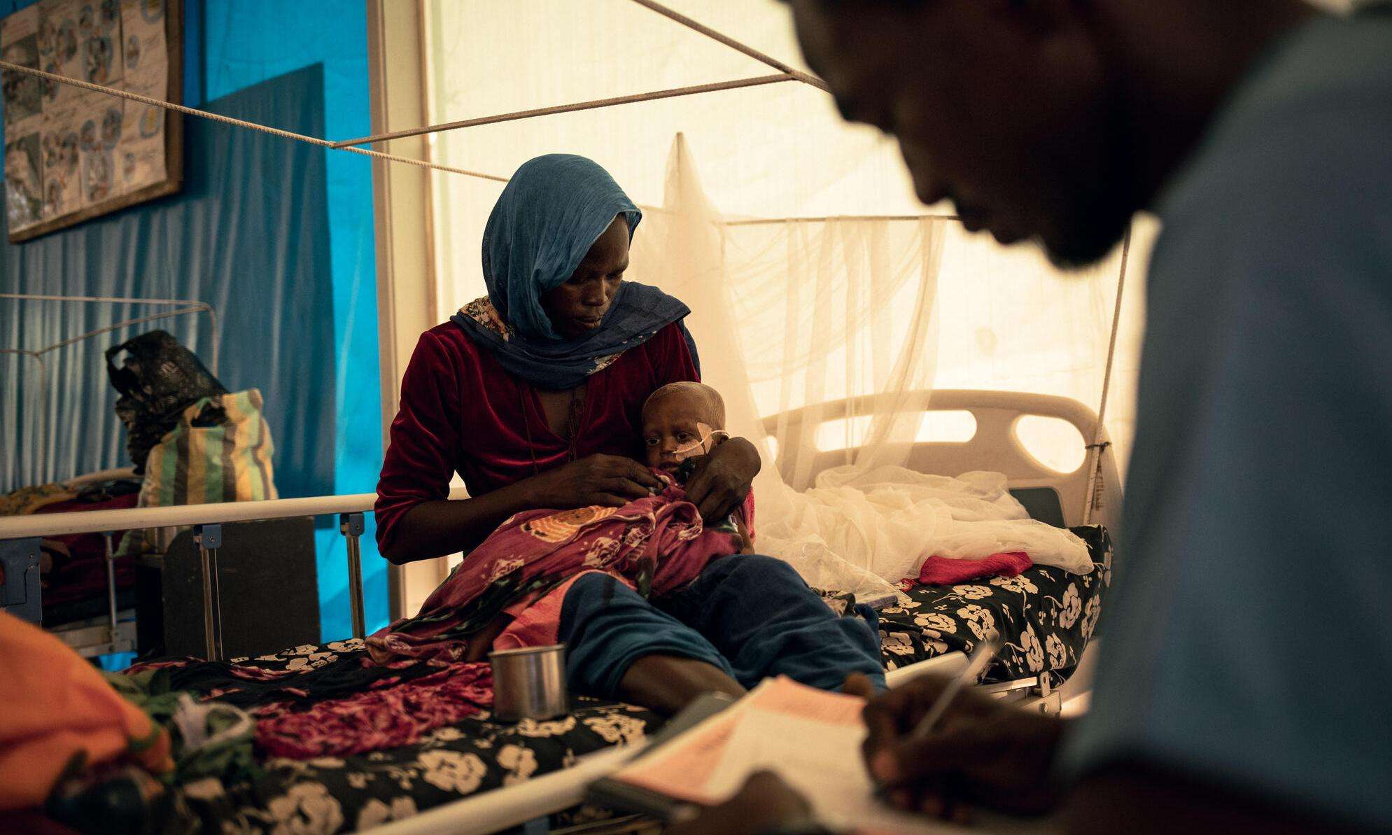 A woman holds her infant son on her lap in a hospital bed in Chad. 