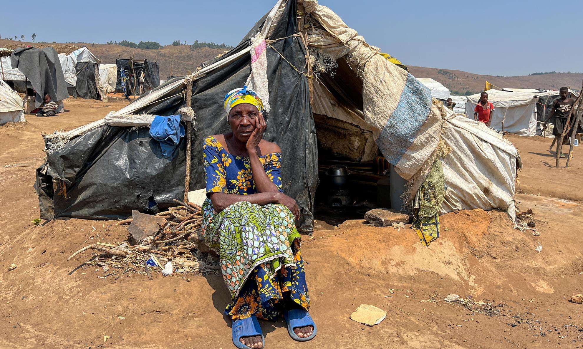 A woman sitting in front of a tent looks at camera in Burundi. 