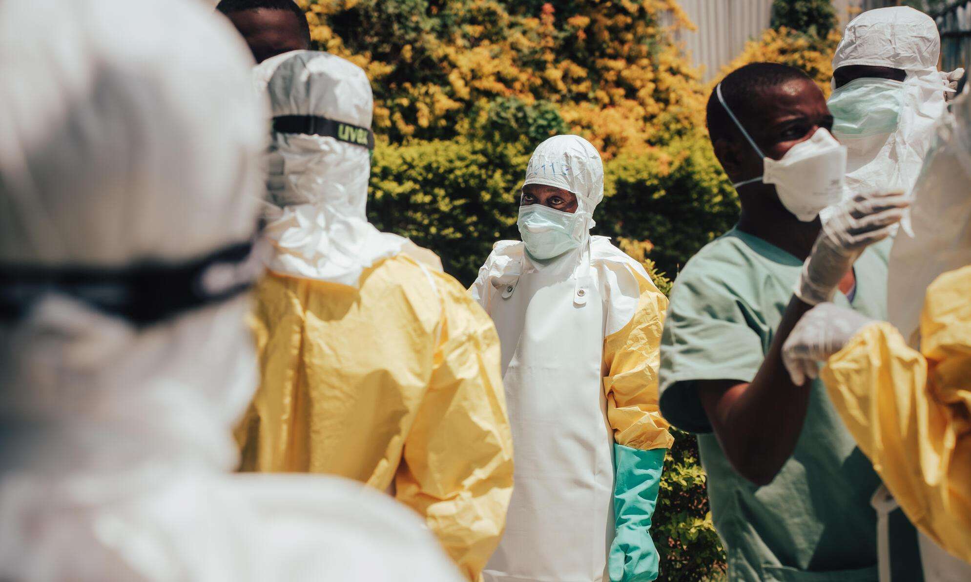 Colleagues help one another into their personal protective equipment (PPE) before decontaminating homes in Bunia, Ituri province, DR Congo.