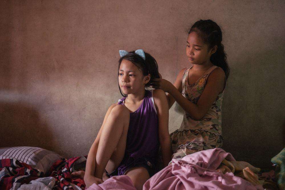 Young girls Elyes and Diana fix each other's hair before posing for a portrait in their tenement home near Smokey Mountain, Manila