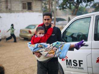 A Palestinian man carries an injured child in a blanket near an MSF vehicle in Rafah, Gaza.