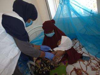 MSF staff member in surgical mask and white vest administers an injection to a baby held by its mother in Somalia.