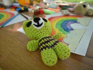 green knit toy lays on wooden table with drawing of a rainbow