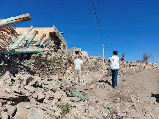 Two people with MSF logos on their shirts walking amidst the concrete wreckage of the earthquake.