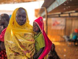A woman in a yellow scarf and her child who are internally displaced in Sudan due to the current conflict.