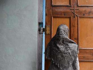 The back of an MSF patient wearing a shawl, standing in front of a wooden door in Belgorod, Russia.