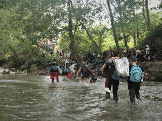 People migrating north walk across a river in the Darién Gap between Colombia and Panama.