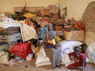 A displaced woman and child sitting in a room full of luggage in Sudan.