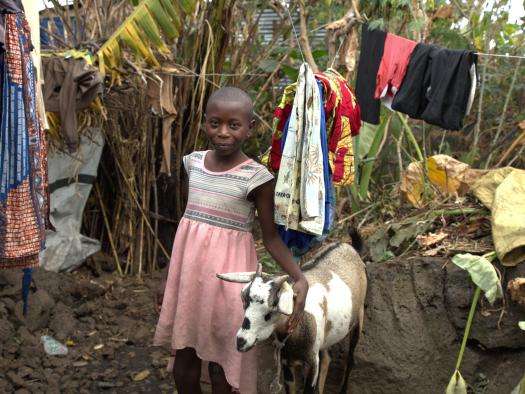 A girl stands next to a goat and smiles at the camera in DR Congo. 