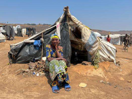 A woman sitting in front of a tent looks at camera in Burundi. 