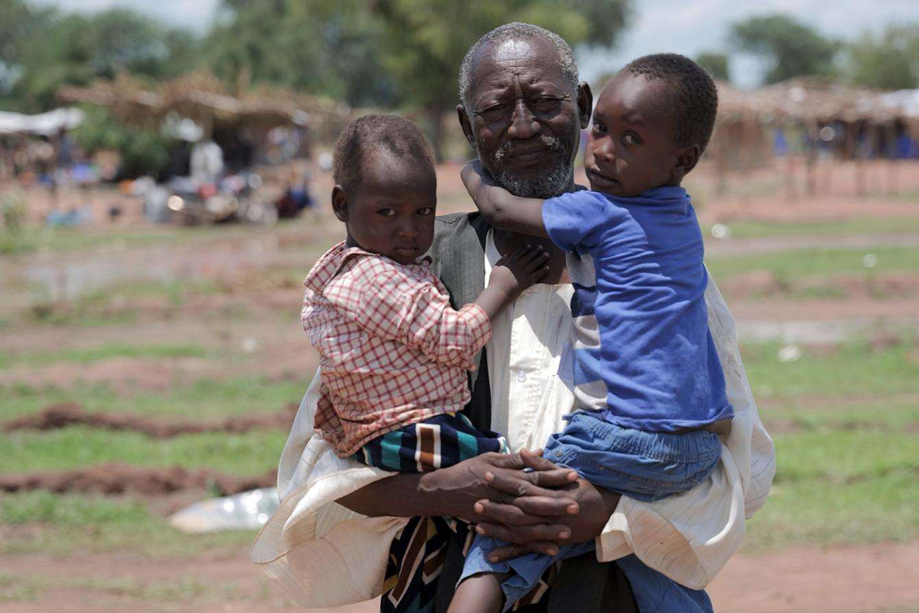 An elderly man holds his two small grandchildren in his arms outside Wedweil refugee camp in South Sudan.