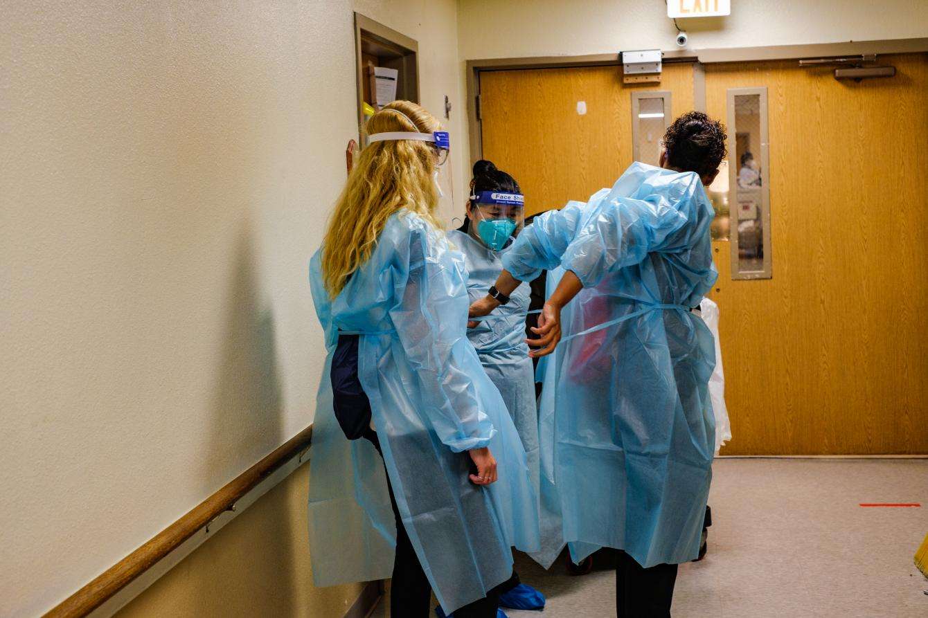 Three medics standing in a hallway, putting on personal protective equipment. 