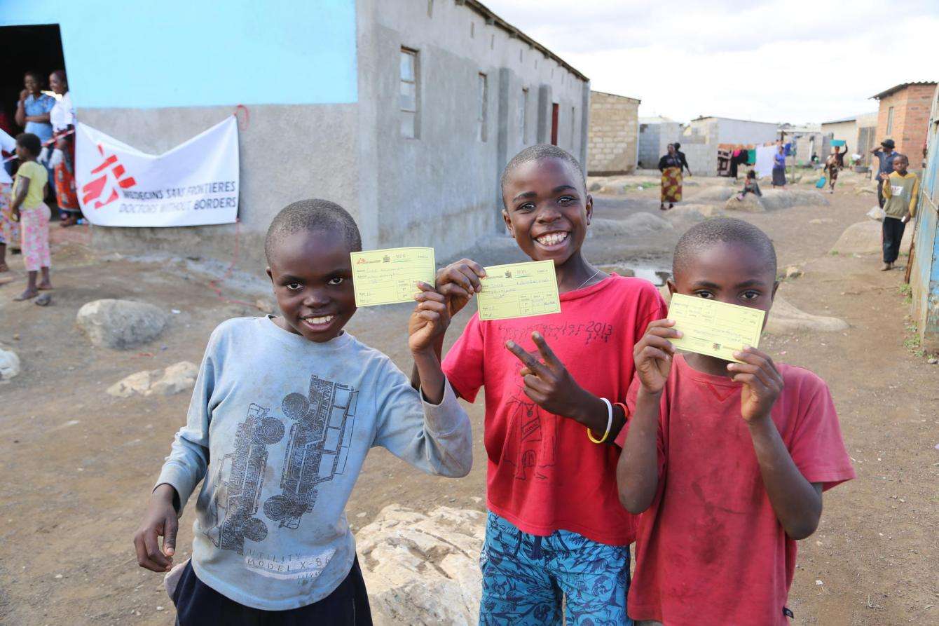 children show their vaccination cards, proof that they have been immunized against cholera
