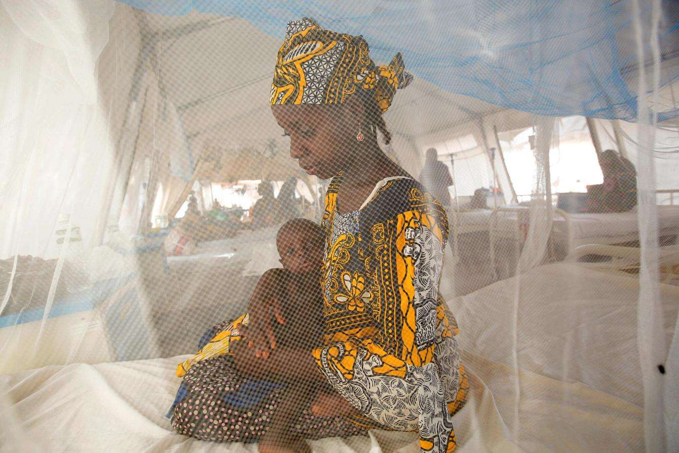 A woman and child sit on a hospital bed behind a mosquito net in Nigeria