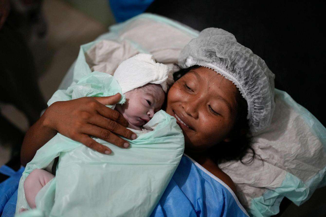 A woman holds newborn baby in hospital bed in Indigenous community in Venezuela