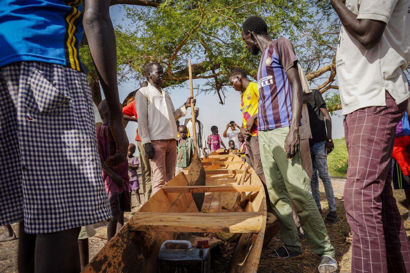 A group of men look at a wooden canoe in South Sudan village preparing for floods