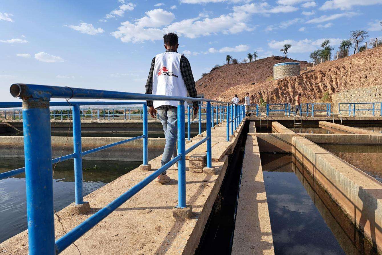 MSF aid worker in white vest walks across a bridge over water at Sheraro treatment plant in Tigray, Ethiopia