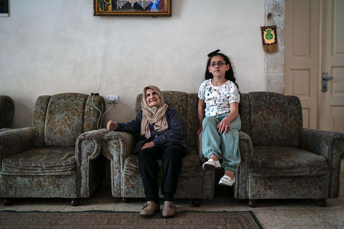 A young girl and her grandmother sit on a couch in their home in Hebron, West Bank, Occupied Palestinian Territories.