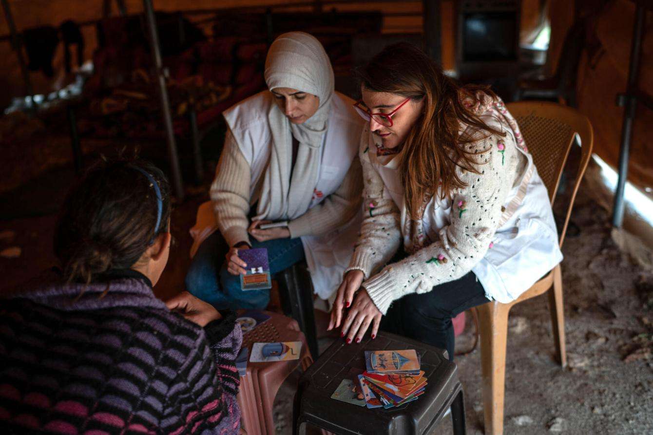 A Palestinian girl and MSF team members in a mental health session in a dark tent the girl is living in after her home was demolished.