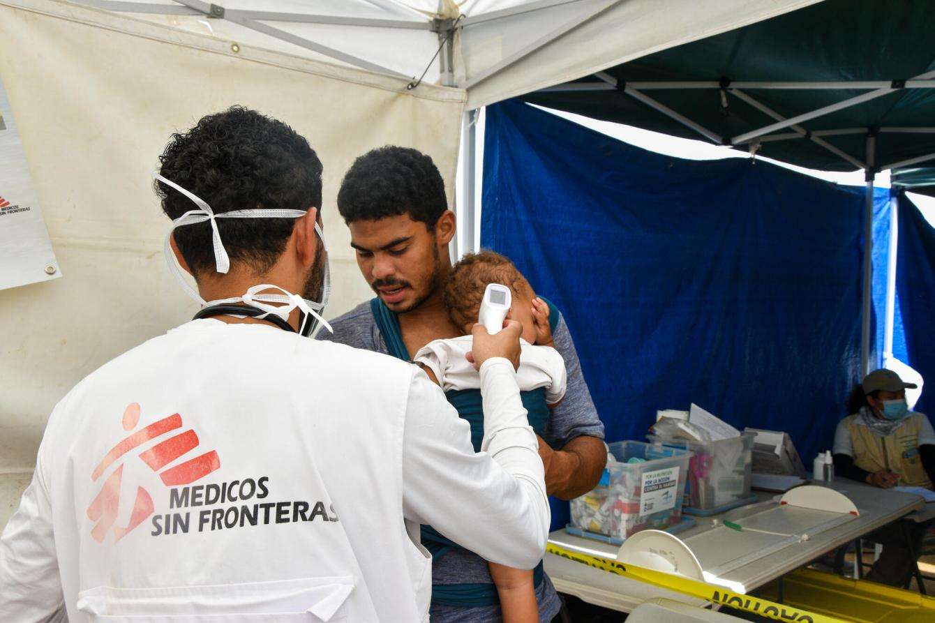 An MSF medic wearing an MSF T-shirt treats a young child being held by a man inside a tent in Danlí, Honduras.