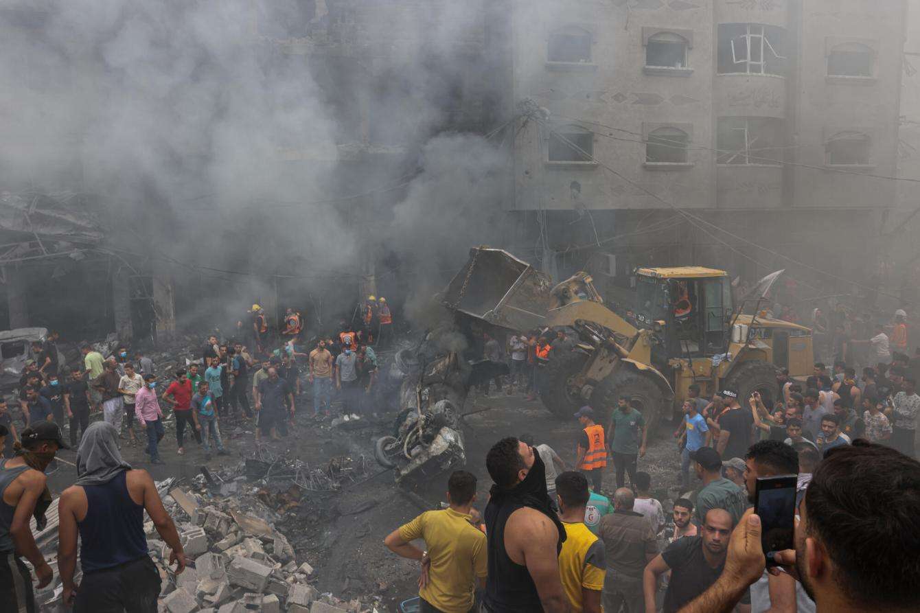 A crowd of Palestinians surrounded by rubble and smoke from Israeli airstrikes in Gaza.
