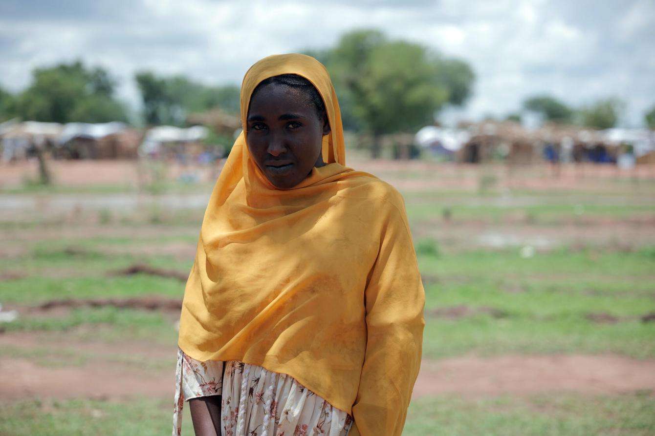 A woman in a yellow scarf stands outside Wedweil refugee settlement in South Sudan.